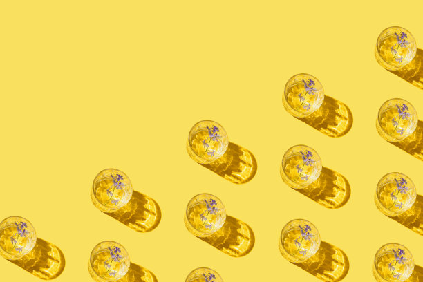 在黄色背景上用玻璃和花水或鸡尾酒制成的创意图案。饮料的概念。最小的风格。前视图。平躺图片下载