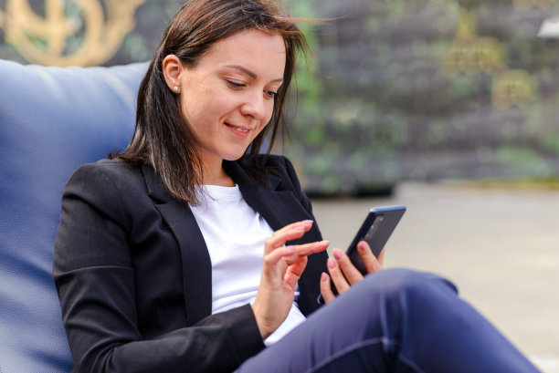年轻的商业女性在户外的咖啡馆使用智能手机的画像。漂亮女孩用网上商务电话，坐在豆袋椅上。白人女性创业，中小企业电话销售工作。图片下载