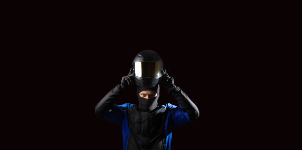 骑摩托车的人穿着防护摩托车夹克，戴着手套和头盔，背景是黑色的。头盔防晒板。图片下载
