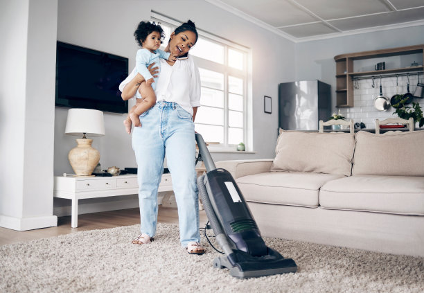 一个年轻的母亲在家里一边用手机一边做家务，抱着她的孩子图片下载