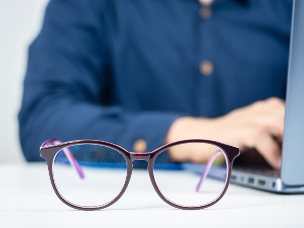 把眼镜放在桌子上，男人在后面用笔记本电脑工作图片下载