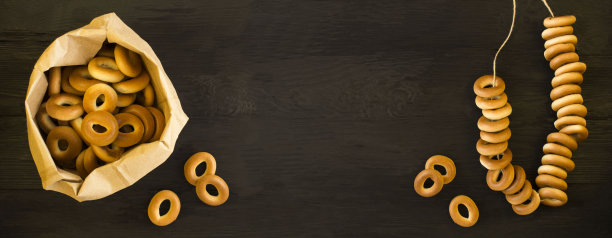 纸包装的百吉饼和黑色木制背景上的一堆百吉饼。前视图。副本的空间。图片下载