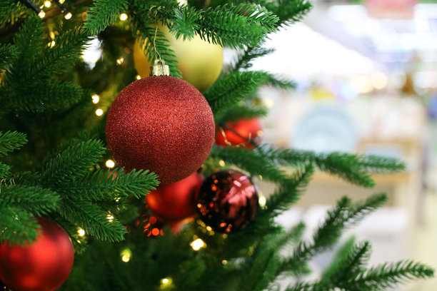商场里挂着红色和金色玩具的圣诞树，背景是模糊的节日彩灯图片下载