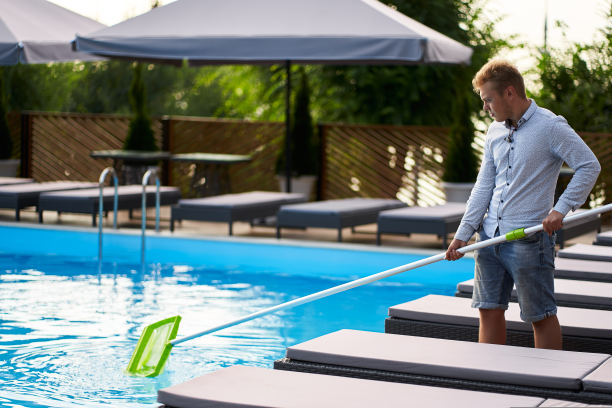 男子带着撇网设备清理游泳池的垃圾。池的服务和维护。雄鱼用树液清除水中的垃圾。游泳池清洁服务。酒店清洁。图片下载