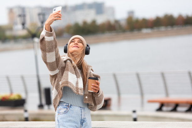 秋天，一名年轻女子在户外散步时用智能手机自拍。图片下载