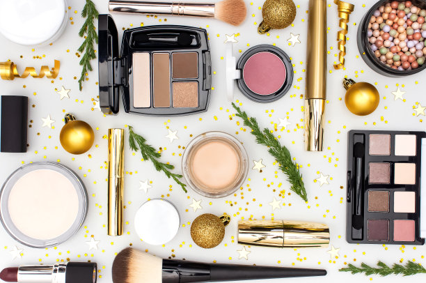 化妆，睫毛膏，粉底霜，口红，眼影，腮红球和新年装饰品，金色的圣诞球，五彩纸屑，星星，杉木树枝，在浅色背景平铺俯视图。化妆品、节日圣诞节图片下载