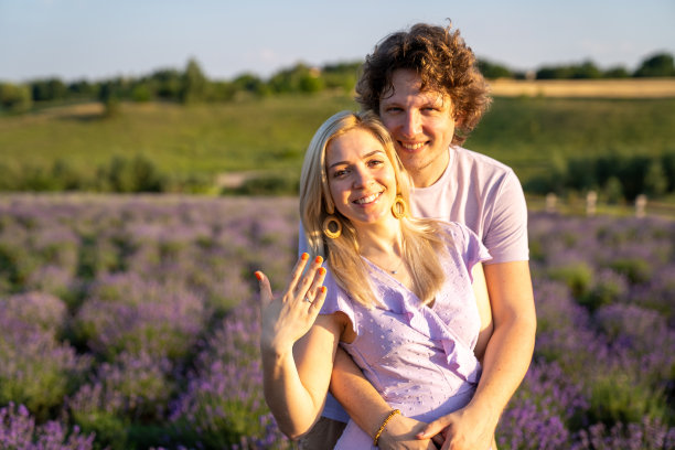 肖像情侣在紫色的丁香相配的衣服拥抱在薰衣草田，浪漫的照片会议，男人和女人在爱，幸福的关系，丈夫和妻子，伙伴刚刚订婚，女人正在展示新的订婚戒指在手上，温柔图片下载