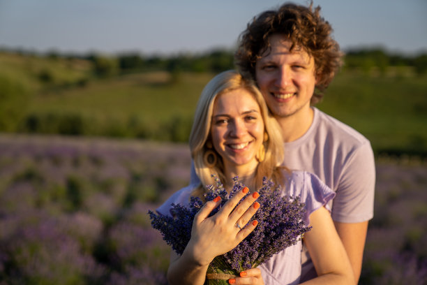 肖像情侣在紫色的丁香相配的衣服拥抱在薰衣草田，浪漫的照片会议，男人和女人在爱，幸福的关系，丈夫和妻子，伙伴刚刚订婚，女人正在展示新的订婚戒指在手上，温柔图片下载