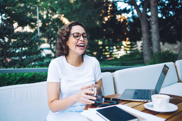 坐在户外咖啡馆里拿着笔记本电脑大笑的女人图片下载