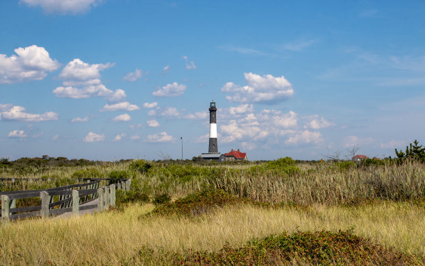火岛灯塔的背景，非常干燥的海滩草和前景的木板路图片下载