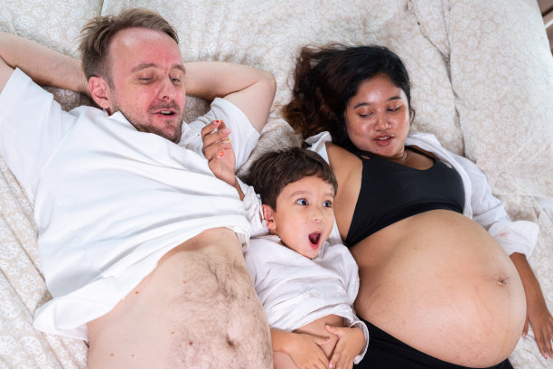 年轻快乐、积极微笑的夫妇怀孕的妻子和丈夫和他们的儿子在床上放松的照片图片下载