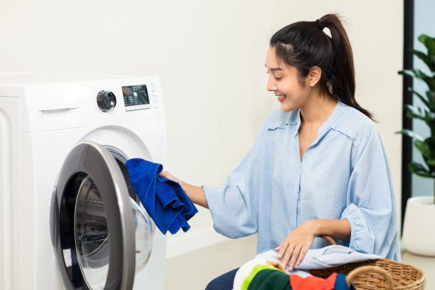 快乐美丽的家庭主妇打开洗衣机的前面，准备在周末把脏衣服放进洗衣机。清洗衣服的女人。图片下载