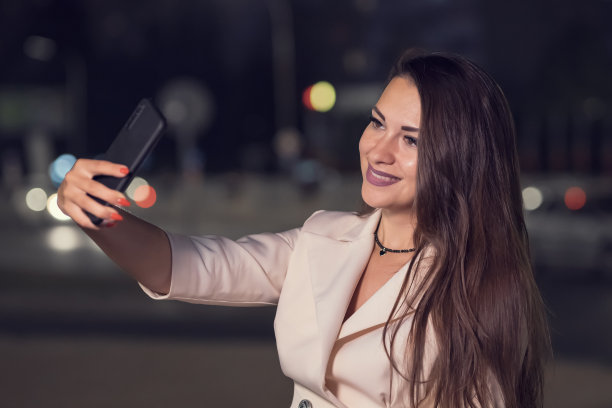 成年女子在夜晚的街道上用手机做鬼脸自拍图片下载