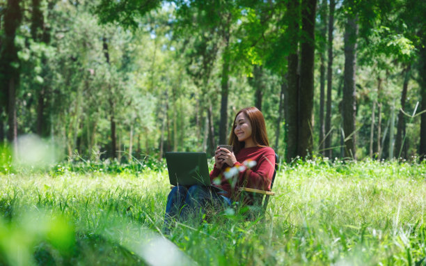 一位美丽的亚洲女性坐在公园的椅子上，一边喝着咖啡，一边用笔记本电脑键盘工作图片下载