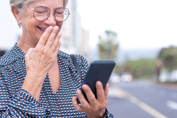 肖像资深自信的白人女商人站在户外的城市街道上使用手机和大笑图片下载