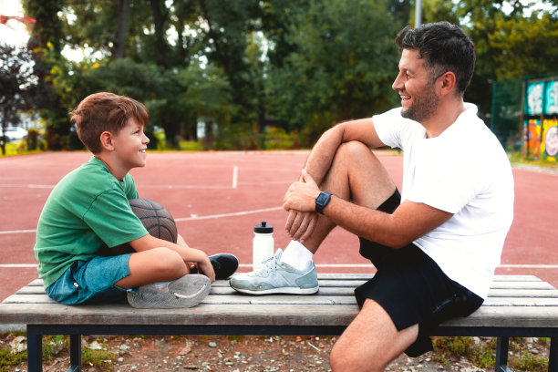 父亲和儿子打完篮球后正在休息。年轻人和十几岁的男孩聊天喝水图片下载