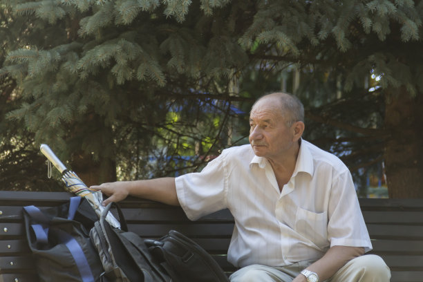 一位老人坐在公园里的长凳上休息，公园里有树和花。爷爷已经退休了。图片下载