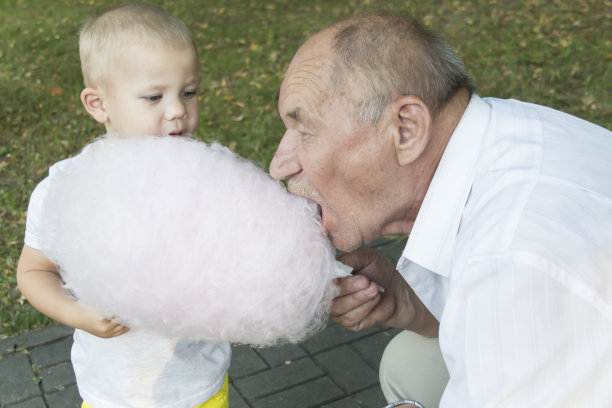 一个上了年纪的男人张大嘴巴贪婪地咬着棉花糖。孙子在爷爷旁边吃棉花糖。图片下载