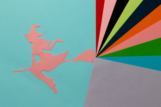 粉色纸上女巫的剪影在蓝色部分的背景上，从她的扫帚出来的彩色艺术部分的背景，万圣节的概念，平铺，纸工艺品图片下载