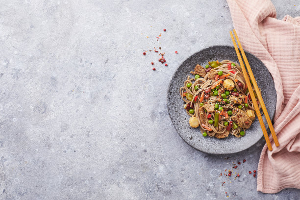 锅里有火鸡肉，荞麦面，玉米，青豆，青豆和胡萝卜，用筷子夹在灰色的背景上。亚洲美食，街头小吃的概念图片下载