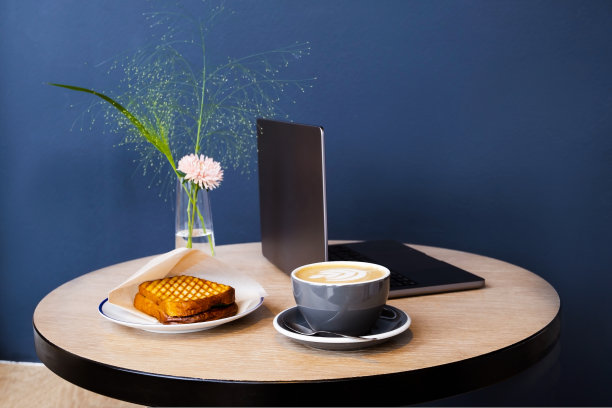 在联合办公空间或办公室的工作场所。一台笔记本电脑，一杯咖啡和一个三明治来补充能量。蓝灰色背景图片下载