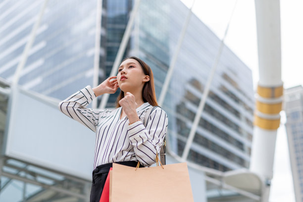 迷人、优雅、聪明的亚洲女商人女雇员在曼谷市中心商业区疯狂购物后，拿着棕色和红色的纸购物袋时尚地摆姿势图片下载