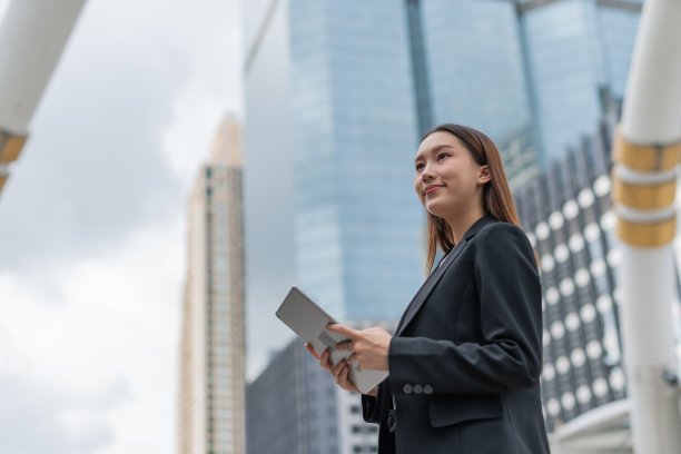 在曼谷市中心的一个商务区，年轻迷人的亚洲职业女商人女士带着美好的微笑在她的平板电脑上阅读了最新的市场和销售报告后仰望天空图片下载
