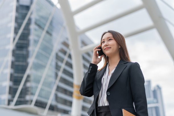 迷人的年轻亚洲职业女商人女士，脸上带着美好的微笑，一边走路一边拿着夹夹板在曼谷市中心商业区打电话图片下载