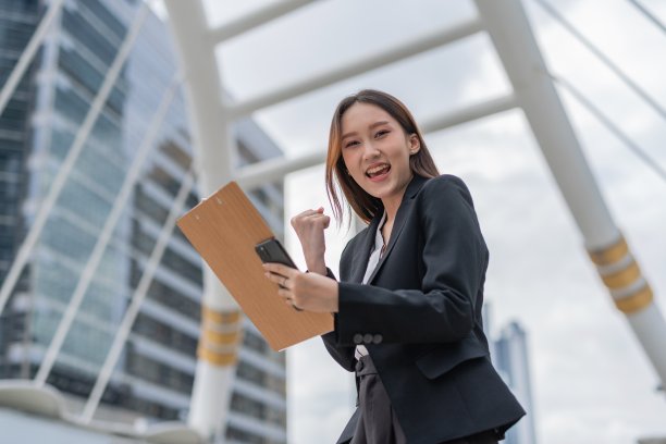 迷人的年轻亚洲职业女商人女士与狂喜的情绪是的，在曼谷市中心商业区看完最新的良好销售报告后看着相机图片下载
