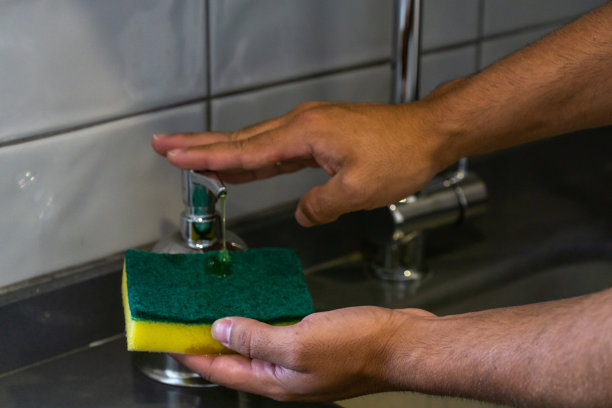 一个面目全非的年轻白人男子拿着一个洗涤垫，在家里倒肥皂洗碗图片下载