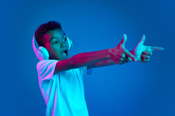 6-7岁的小男孩，穿着白色t恤，戴着耳机，在霓虹灯下听着蓝色背景的音乐。图片下载