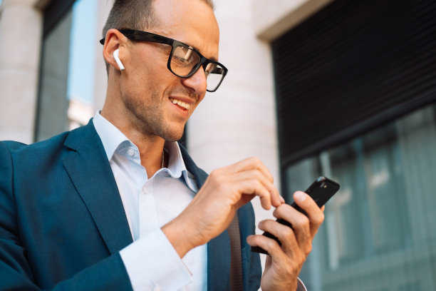 年轻的商人在城市里用智能手机开心地笑着。图片下载