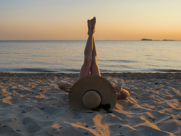 日落时分的沙滩上，一个穿着红色泳衣、戴着帽子的迷人女子图片下载