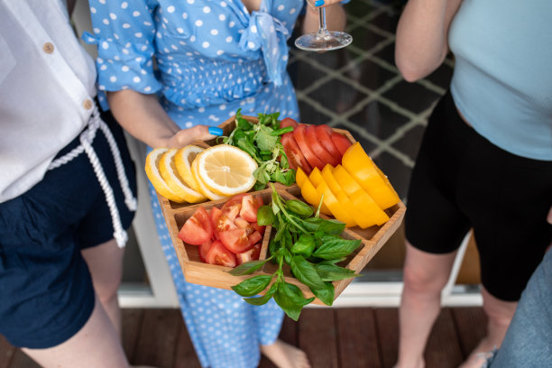 年轻女子拿着切好的蔬菜在木托盘，一杯白葡萄酒，站在房子附近的裁剪照片。前视图。图片下载