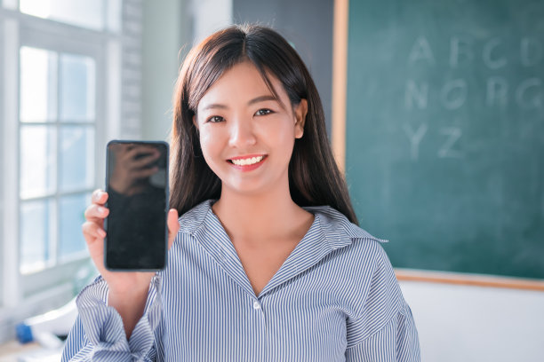 亚洲女教师站在黑板前展示课堂教育广告智能手机屏幕，教育在线概念。图片下载