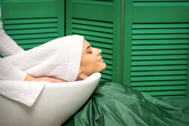 一位年轻的白人妇女在理发店洗完头后，理发师用白毛巾把头发裹起来。图片下载