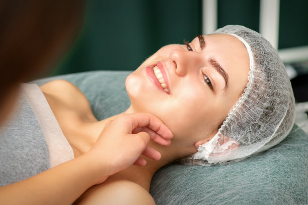 整形外科与美容概念。美容师的手检查和触摸美丽的年轻微笑的白人妇女的脸。图片下载