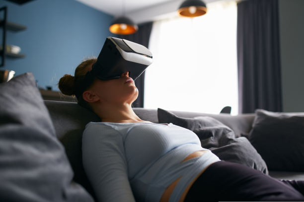 戴着虚拟现实眼镜的女子，通过耳机接口，在极简的室内沙发上休息，进入元世界沉浸式体验。女孩在网络空间玩游戏。未来的概念。图片下载