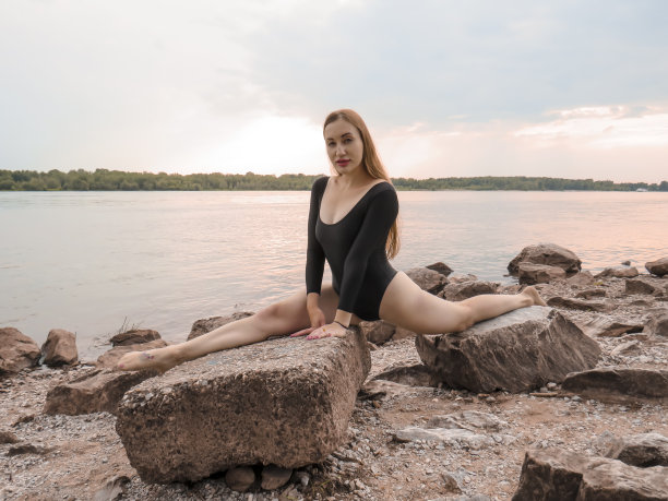 一位身穿黑色运动泳衣的年轻女体操运动员在河岸上进行体育锻炼图片下载