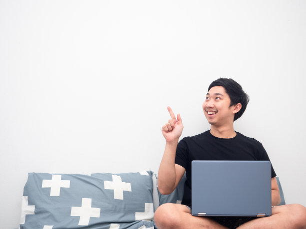带着笔记本电脑坐在床上的亚洲人指着复印空间图片下载