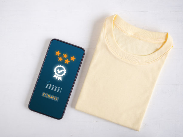 从智能手机的俯视图可以看到一个五星评级的屏幕。产品评论黄色t恤在白色木制背景。图片下载