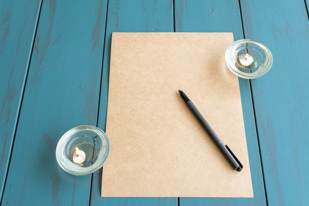 棕色纸上的钢笔，旁边是点燃的蜡烛——正面。图片下载
