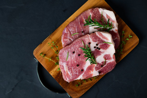 猪肉片配上迷迭香和百里香叶，放在木盘上，图片下载