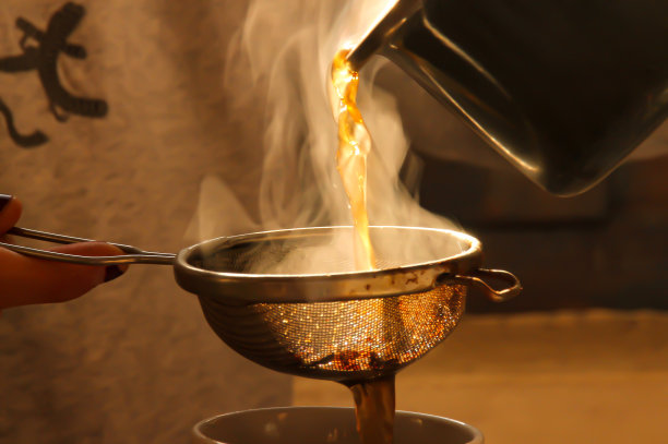 把热茶倒进有过滤网的杯子里，热气腾腾。图片下载