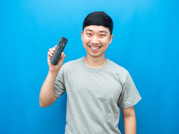 亚洲男子拿着遥控电视与微笑的蓝色背景图片下载