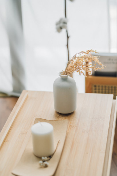 树枝蓬松的米色潘帕斯草在小白色花瓶和蜡烛在木桌上的光背景图片下载