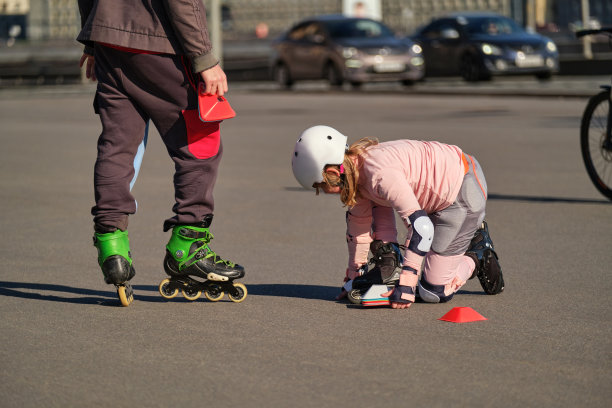 一个十岁的小女孩在街上接受轮滑教练的训练。这孩子和他父亲一起在户外运动。戴着头盔，护膝，护肘的女运动员图片下载