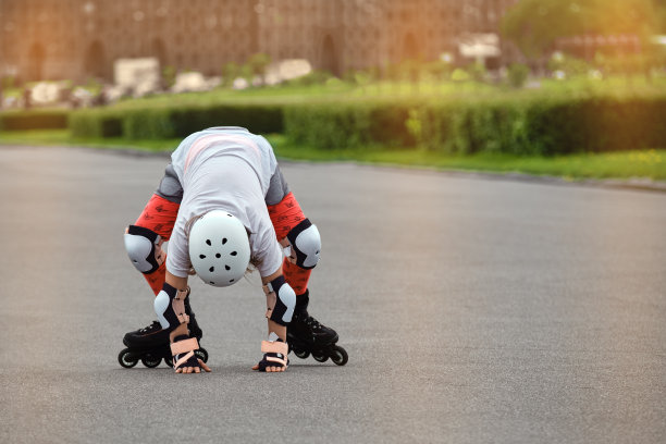 快乐的女孩在公园里学习溜冰。孩子们穿着防摔火车在户外玩溜冰鞋。运动员摔倒后爬起来图片下载