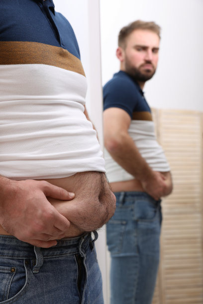 穿着紧身t恤的年轻人在家里的镜子前。超重的问题图片下载