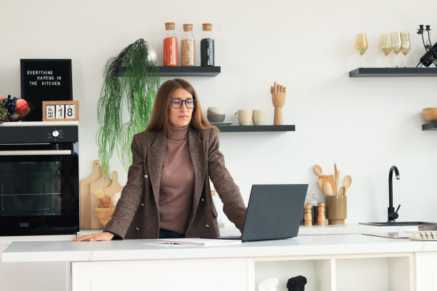 厨房里拿着笔记本电脑的女商人。轻现代装修和女孩站起来，在去上班前思考一些事情图片下载